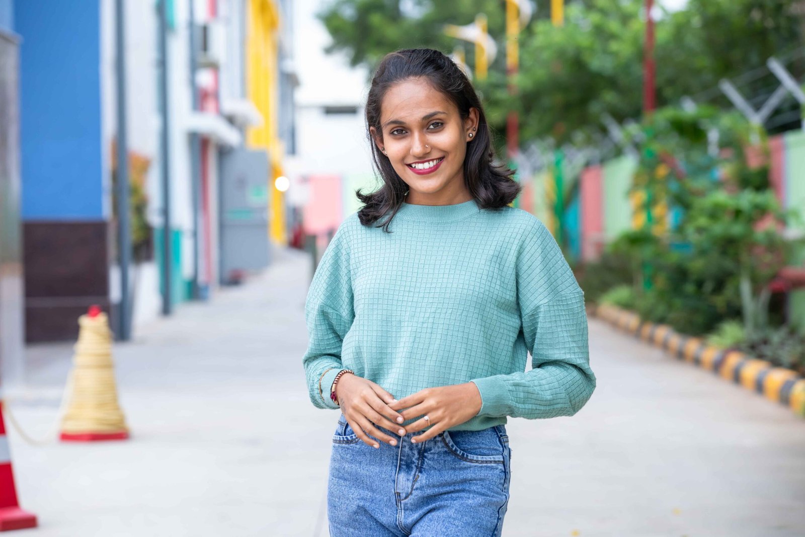Cheerful young woman in casual attire standing on a colorful urban street. Capturing a warm and inviting moment.